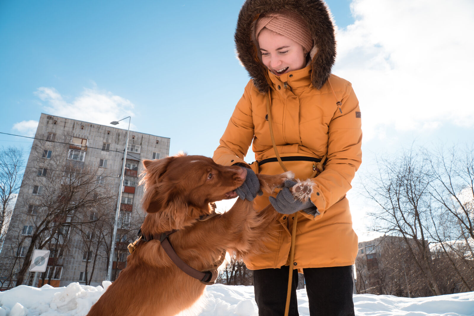 Kobieta ubrana w kurtkę zimową trzyma psa za łapy.