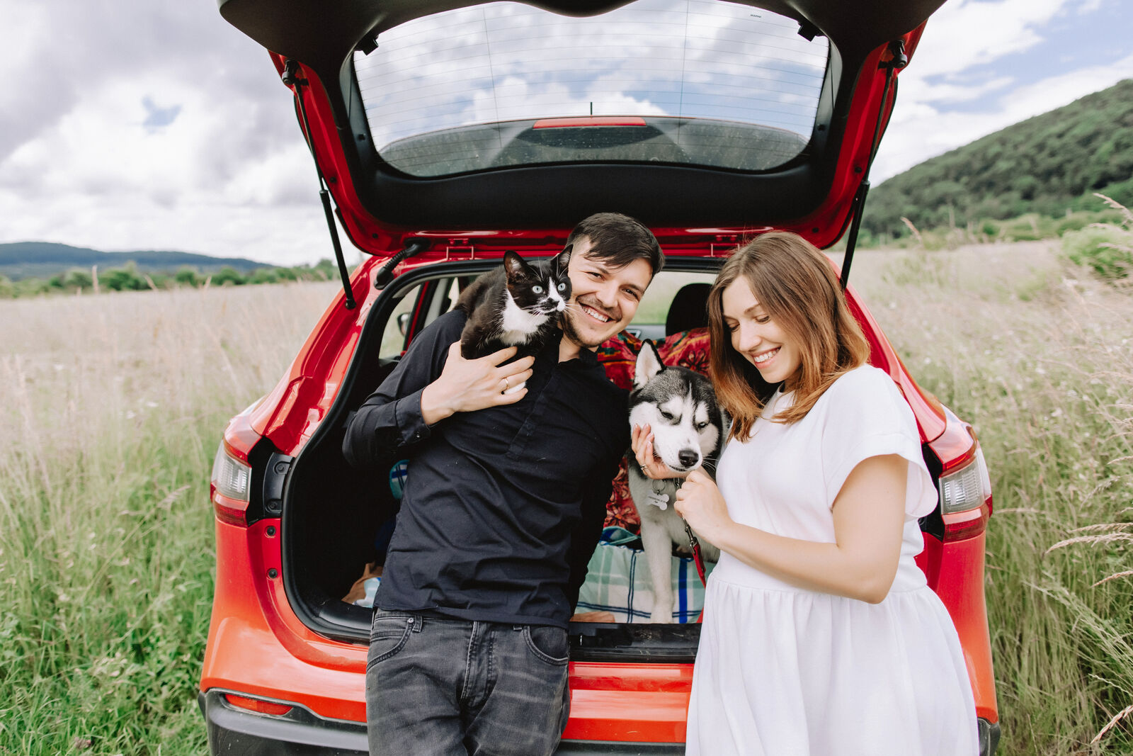 Kobieta i mężczyzna stoją oparci o otwarty bagażnik auta i trzymają swoje zwierzęta.